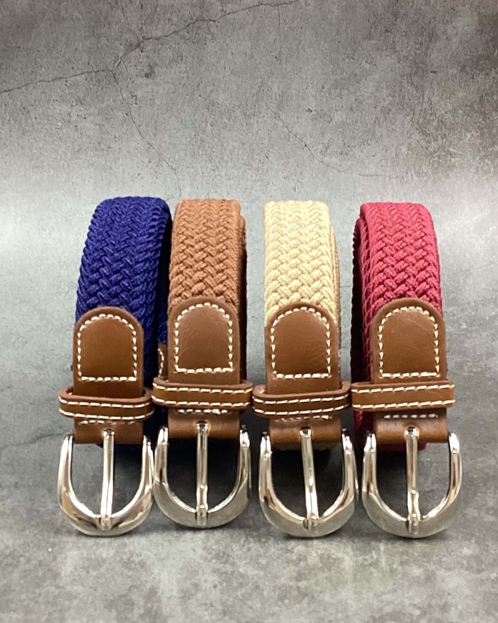 Four 20 mm braided stretch belts in navy, tan, beige and raspberry with brown tabs and pin buckles