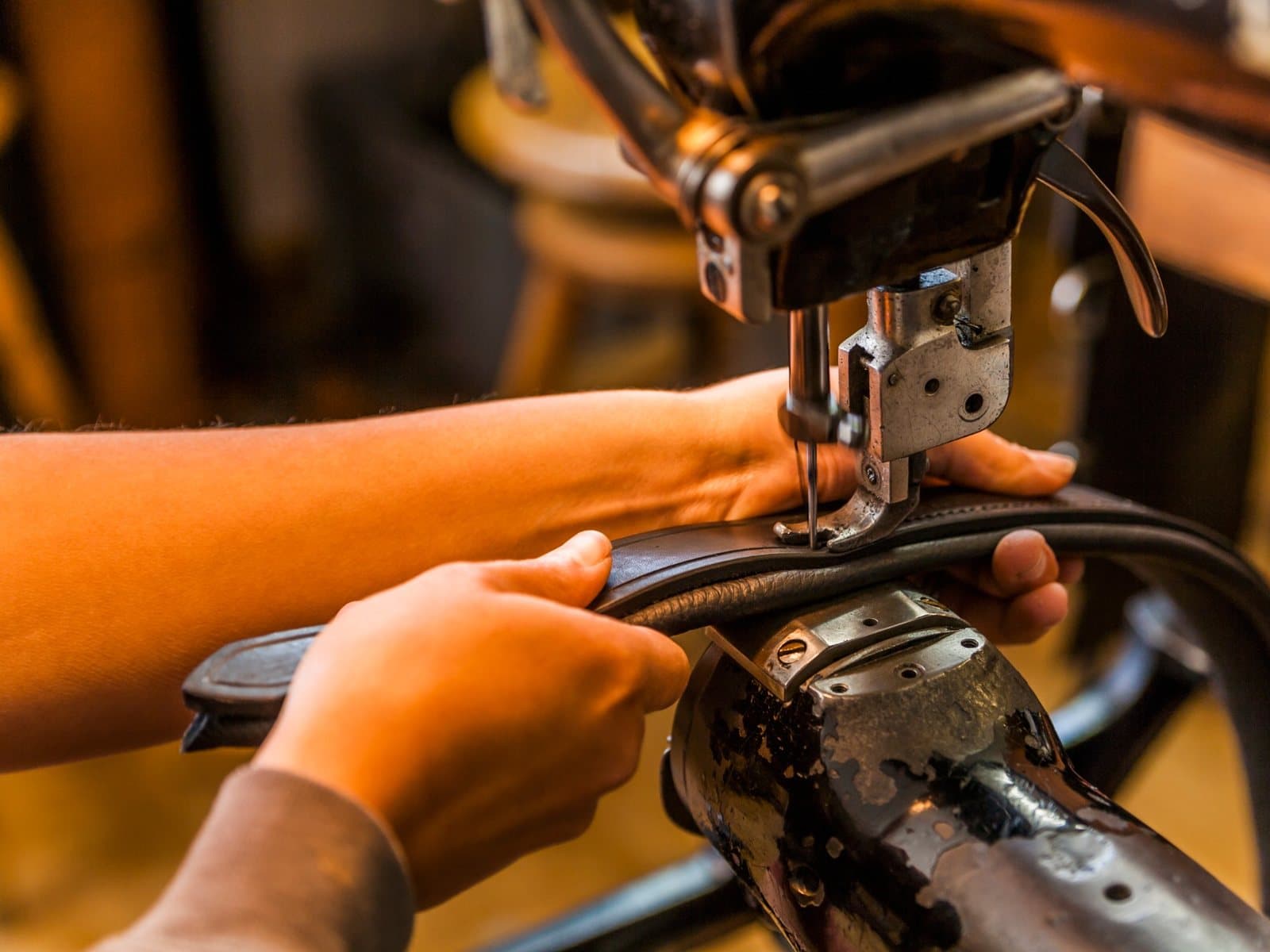 A craftsman's hands guiding a leather belt under the needle of a sewing machine
